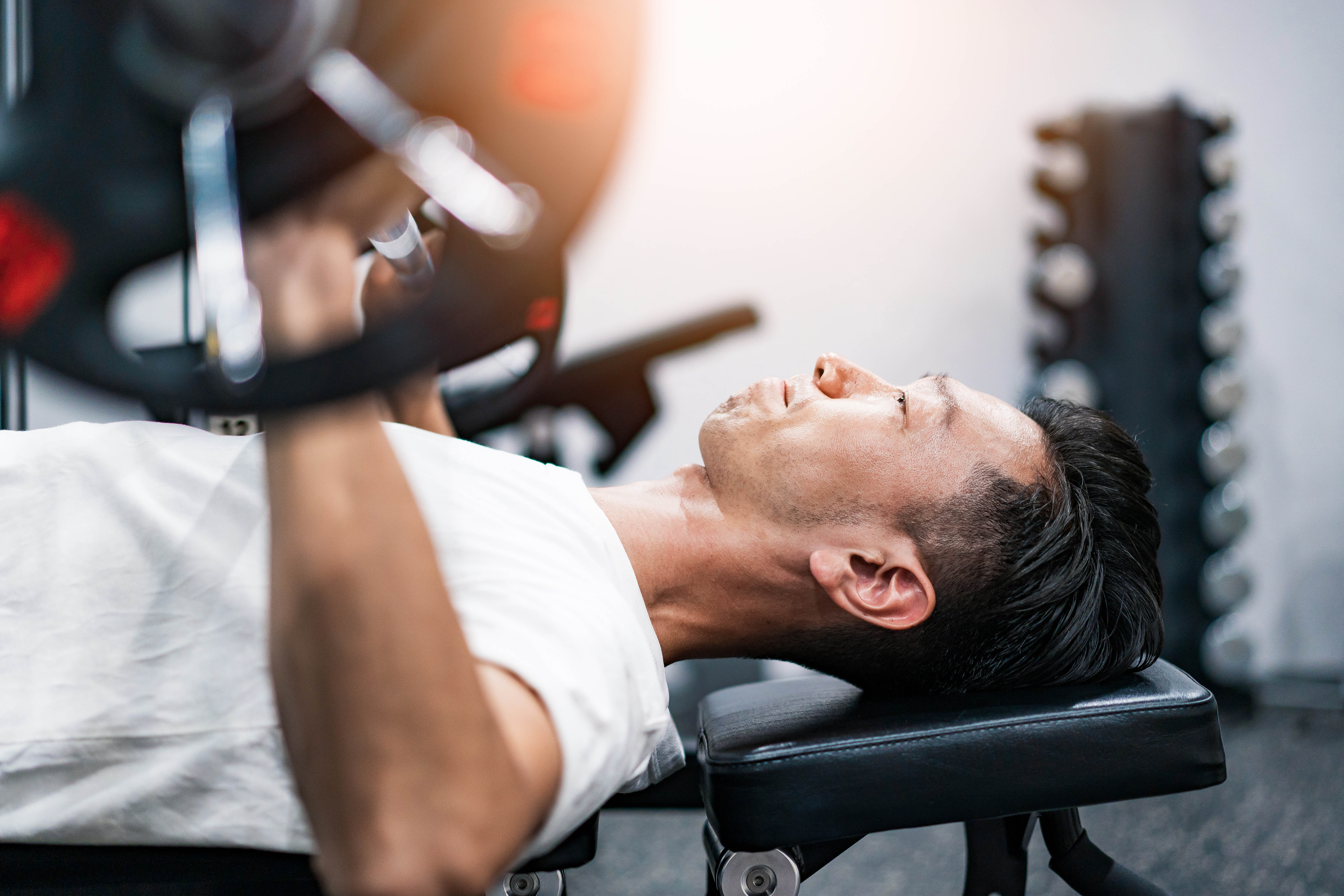 Middle aged Asian man laying on a bench in the gym, preparing to do a chest press Middle aged Asian man laying on a bench in the gym, preparing to do a chest press